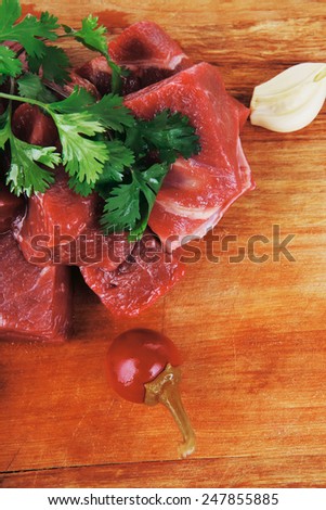 uncooked fresh beef meat chunks on wooden cutting plate with green hot and red peppers isolated over white background