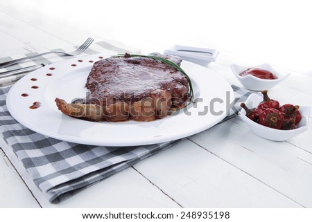 fresh rich juicy grilled beef meat steak fillet on white plate over wooden table decorated with sauces and cutlery new york style