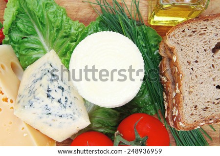 fresh aged french cheeses chops on big cutting board with tomatoes olive oil, rye bread and green chives isolated over white background