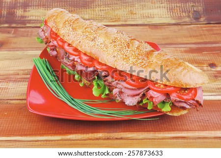 french sandwich on red plate : baguette with smoked sausage over wooden table