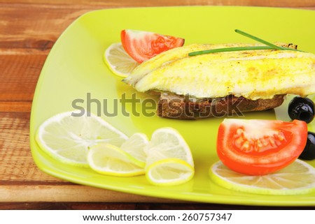 roast fish fillet with tomatoes,chives and bread on plate over wood