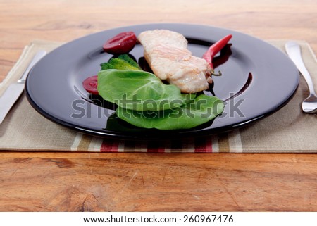 fresh roast turkey meat steak fillet with red hot pepper and green lettuce salad kale on black plate over wooden table with knife and fork