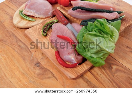 fresh raw turkey meat steak fillet with vegetables kale tomatoes lettuce red hot chili pepper and dark olives on cutting board over wooden table