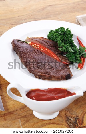 grilled beef steak fillet meat with red hot pepper and  raw kale leaf with ketchup sauce served on white plate over wood table