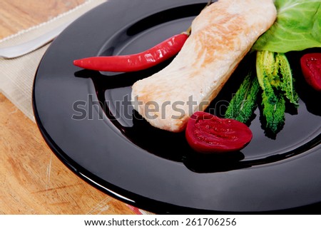 fresh roast turkey meat steak fillet with red hot pepper and green lettuce salad kale on black plate over wooden table with knife and fork