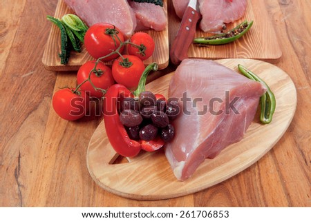 fersh raw turkey meat steak fillet with vegetables kale tomatoes lettuce red hot chili pepper and dark olives on cutting board over wooden table
