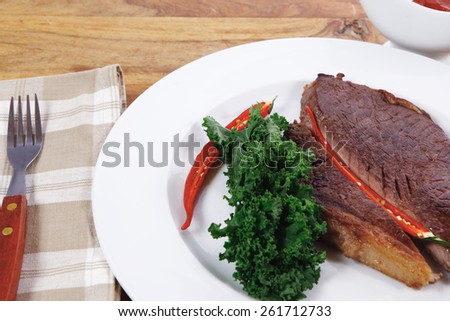 grilled beef steak fillet meat with red hot pepper and  raw kale leaf with ketchup sauce served on white plate over wood table
