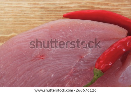 raw fresh turkey meat steak fillet cuts on wooden board with red hot chili pepper isolated over white background