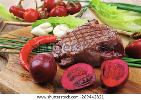 meat food : roast beef garnished with green staff and red chili hot pepper on wooden table with cutlery