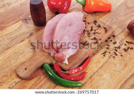 fresh raw turkey meat steak with hot sweet pepper dry spices castor and pepperbox on wood cutting boar over table