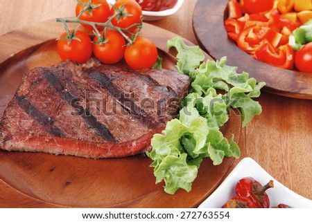 fresh rich juicy grilled beef meat steak fillet with marks on wooden plate over table decorated with lettuce salad and cutlery, new york styled cuisine