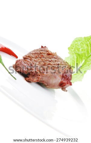 meat food : roast beef steak garnished with green lettuce and red chili hot pepper on white plate isolated over white background