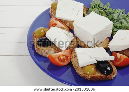 white feta greek cheese sandwich rye bread on blue plate with black spain olives tomatoes and cutlery over retro wooden table