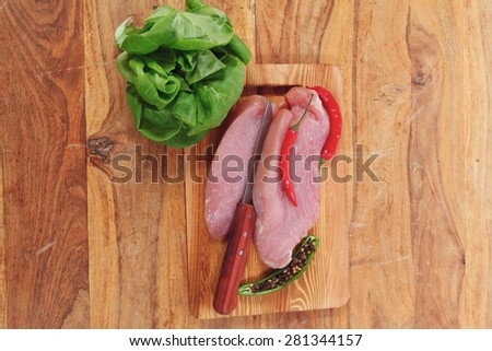 fresh raw turkey steak fillet with red hot chili pepper and green salad on cutting board over wooden table