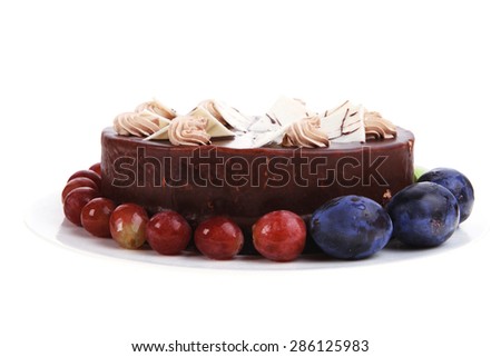 chocolate cream brownie cake topped with white chocolate slice and cream flowers decorated with fruits apple plum and grape on plate isolated over white background