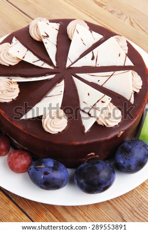 chocolate cream brownie cake topped with white chocolate slice and cream flowers decorated with fruits apple plum and grape on plate on wooden table