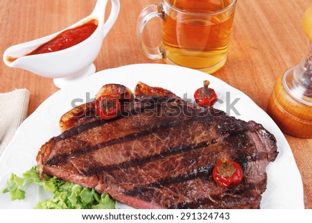 rural design new york meat style beef steak fillet on white plate with hot chili pepper served with tea cup ketchup in Gravy boat pepper mill and cutlery on napkin on wooden table