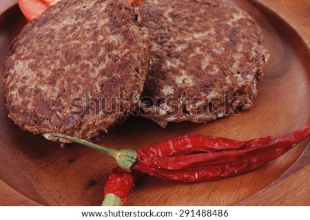 fresh beef meat hamburger on wooden plate with cutlery and rye bread bun on tablecloth with whiskey shot