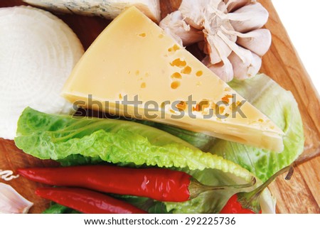 several  delicatessen types of cheese on wooden board with hot peppers and dill isolated on white background