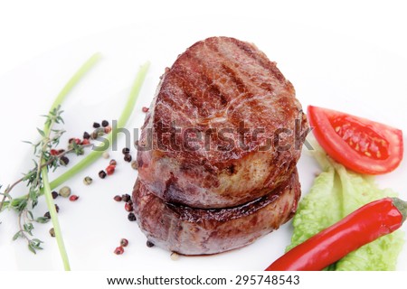 grilled beef fillet medallions on noodles with red hot chili pepper and salad leaf on white plate isolated over white background