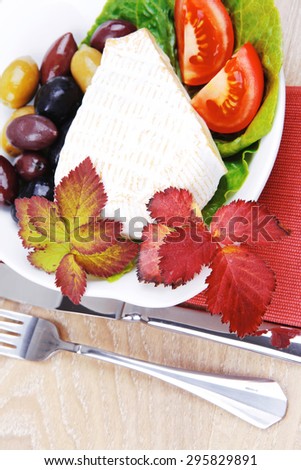 aged camembert cheese on green salad in white dish over cloth with olives and over wooden table
