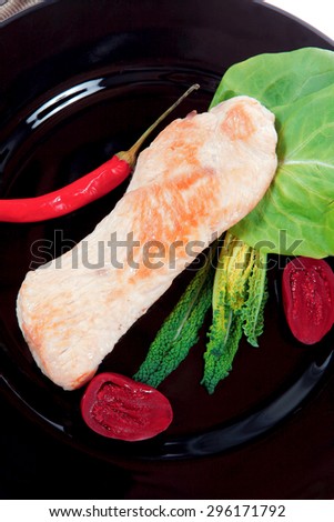 fresh roast turkey meat steak fillet with red hot pepper and green lettuce salad kale on black plate isolated over white background