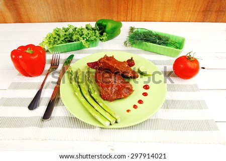 roast stew beef pork meat served with vegetables on green plate and cutlery on napkin over wooden table with red hot peppers