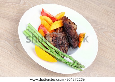 meat food : grilled red beef fillet with mango tomatoes and asparagus , served on white dish over wooden table