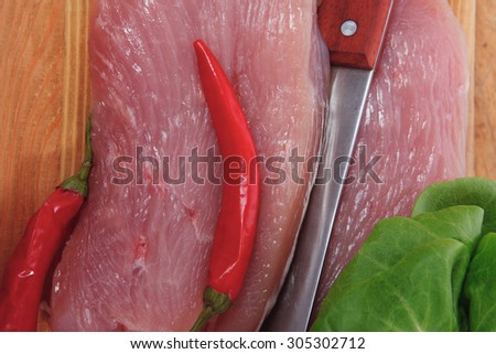 fresh raw turkey steak fillet with red hot chili pepper and green salad on cutting board over wooden table