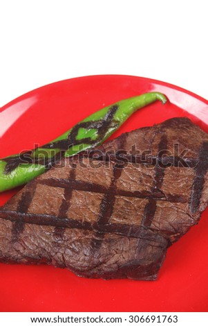 fresh grilled bbq roast beef steak on red plate with green chili pepper isolated on white background