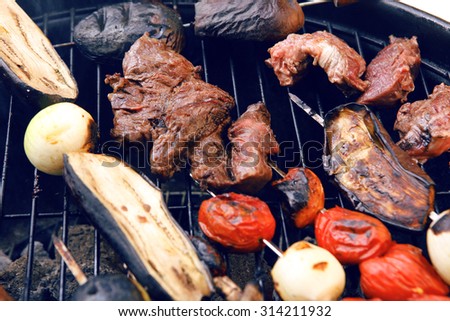fresh raw beef fillet steak red meat with tomatoes and eggplant on skewers on big round barbecue brazier grid full with ready charcoal selective focus dof