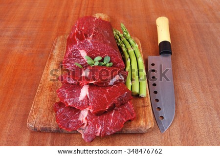 red fresh raw beef veal fillet with asparagus and stainless steel chef knife on cutting plate over wooden table prepared to use