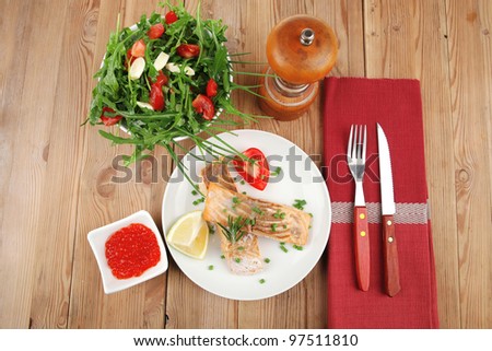 healthy fish cuisine : grilled pink salmon steaks with red caviar in white bowl , lemon and vegetable salad on white dish with cutlery and pepper grinder over wooden table