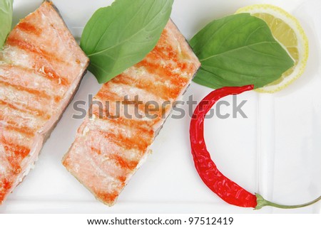grilled sea salmon chunks with pepper and lemon on basil leaf over ceramic plate isolated on white background