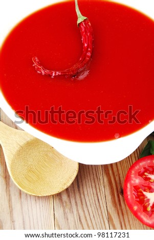 hot fresh diet tomato soup with basil thyme and raw tomatoes in white round bowl over red mat on wood table ready to eat