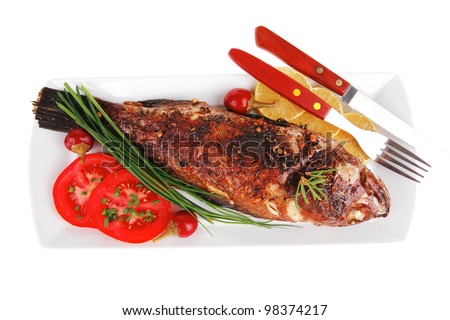 served main course isolated on white: whole fried seabass on plate with lemons,tomatoes and peppers