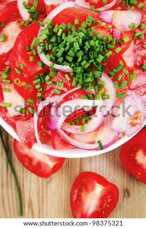 healthy appetizer : fresh tomato salad in white bowl with bunch of chives and raw tomatoes on twig , violet onion, over wooden table