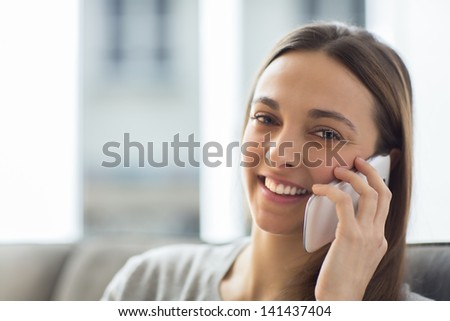 Pretty young female using cell phone at home looking at the camera