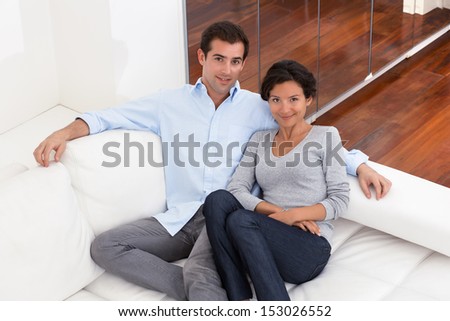 Portrait of smiling young couple on couch at home, looking camera