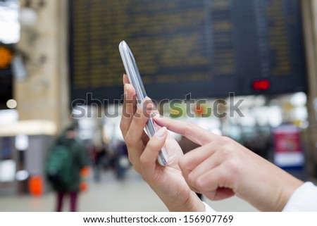 Close up of hands woman using her cell phone in train station, background time display panels