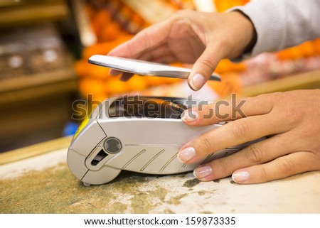 Woman paying with nfc technology on mobile phone in supermarket, electronic reader