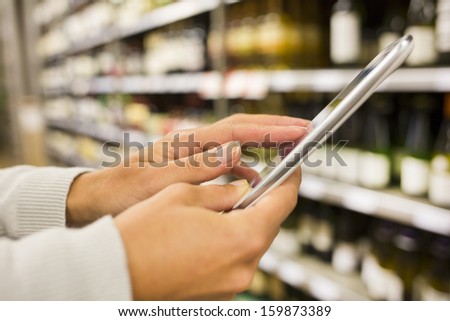Woman using mobile phone while shopping in supermarket, wine department store
