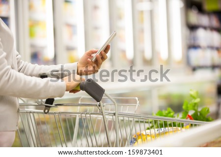 Woman Using Mobile Phone While Shopping In Supermarket, Trolley, Frozen Department Store