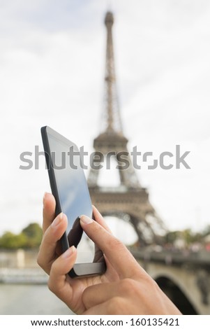 Woman in Paris using her cell phone in front of Eiffel Tower, seine bridge background, message sms e-mail