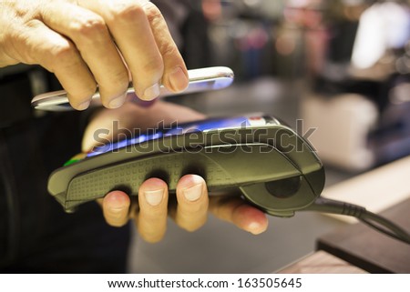 Man paying with NFC technology on Cell Phone, in clothing store