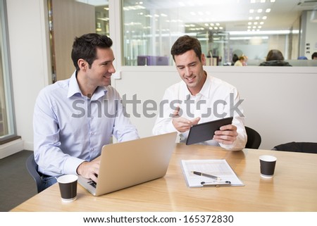 Two casual businessmen working together in modern office with laptop and tablet pc