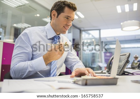 Businessman with laptop eating sushi on his desk