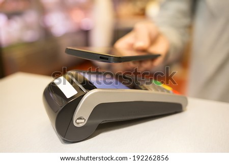 Woman paying with NFC technology on mobile phone, in supermarket