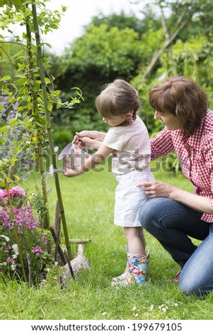 Grandmother with her granddaughter watering flowers in the garden