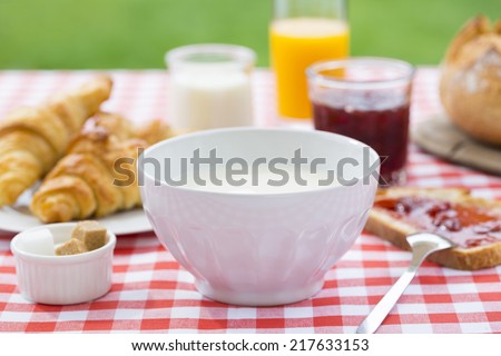Breakfast in garden with hot milk, orange juice, croissant, marmalade and bread.